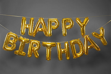 Phrase HAPPY BIRTHDAY made of golden balloon letters on grey background
