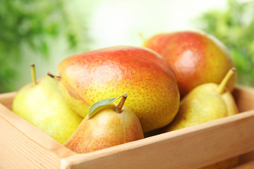Ripe juicy pears in wooden crate against blurred background, closeup