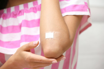 Woman with adhesive bandage on elbow against light background, closeup
