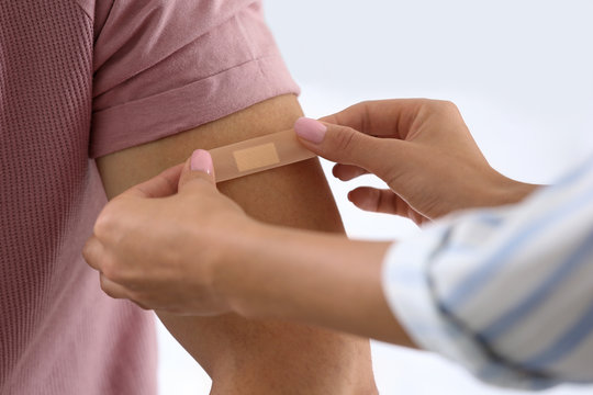 Woman applying adhesive bandage on man's arm against light background, closeup