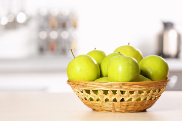 Wicker bowl with sweet green apples on table in kitchen, space for text