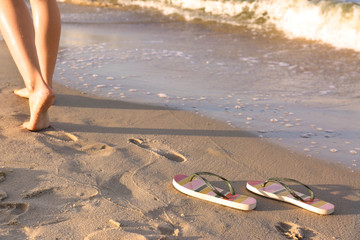 Closeup of woman and flip flops on sand near sea, space for text. Beach accessories
