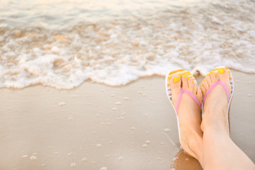 Closeup of woman with stylish flip flops on sand near sea, space for text. Beach accessories