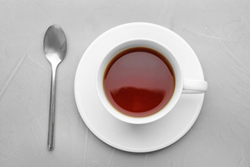 Cup of tea with saucer and spoon on grey background, flat lay