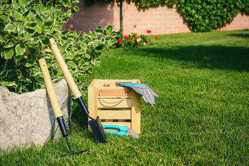 Set of gardening tools and wooden crate on green grass