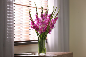 Vase with beautiful pink gladiolus flowers on wooden table in room, space for text