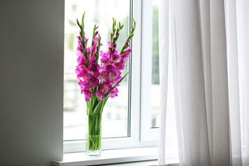 Vase with beautiful pink gladiolus flowers on windowsill, space for text