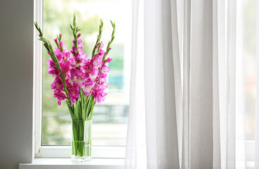 Vase with beautiful pink gladiolus flowers on windowsill, space for text - obrazy, fototapety, plakaty