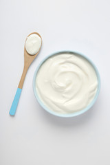 Bowl of sour cream and wooden spoon on white background, top view