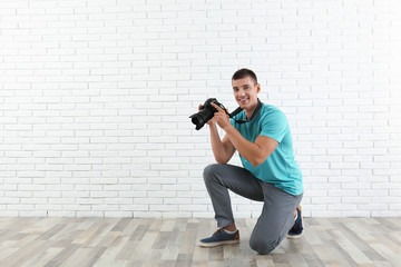 Young photographer with professional camera near brick wall. Space for text