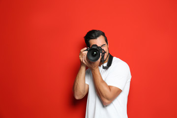 Young professional photographer taking picture on red background. Space for text