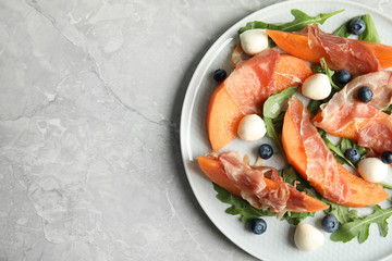 Fresh melon with prosciutto, mozzarella and arugula on light grey table, above view. Space for text
