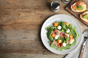 Flat lay composition of fresh melon with prosciutto on wooden table. Space for text