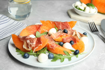 Fresh melon with prosciutto, mozzarella and arugula on light grey table