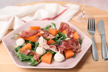 Fresh melon with prosciutto, mozzarella and arugula on wooden table