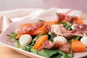 Fresh melon with prosciutto, mozzarella and arugula on plate, closeup