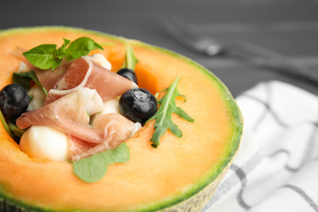 Half of melon with prosciutto, blueberries and herbs on table, closeup