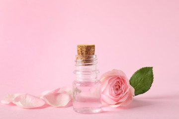Bottle of essential oil and rose on pink background