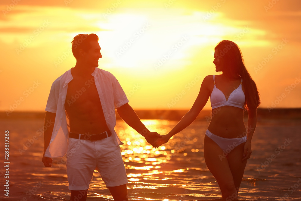 Wall mural happy young couple spending time together on sea beach at sunset