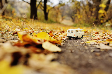 white little toy car rides on the road against the background of autumn yellow trees. Place for text, design blank, copy space, Hello autumn.