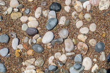 Rounded pebble stones on colorful tiny stones at the beach. Stone background image.