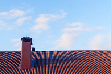 Chimney on the red roof of the house against the blue sky.