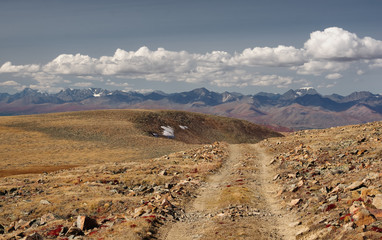 Road through a dry stone desert steppe on a highland mountain plateau with yellow green grass with ranges of hills rocks on a horizon skyline