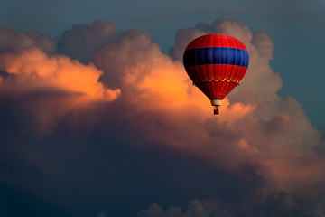 Fantastical image of an ornate red and blue hot air balloon floating high in beautiful storm clouds glowing in purple, pink, yellow, and orange colors at sunset