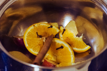 Candid gluhwein cooking at home. Oranges, apples and spices in a pan.