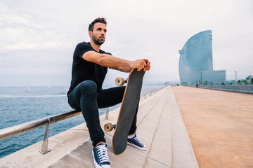 Fototapeta na wymiar Skateboarder sits with skateboard on the modern city sea terrace.