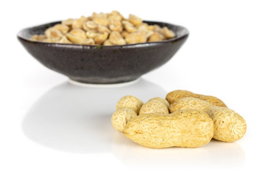 Lot of whole lot of halves of natural yellow peanut few is aside in dark ceramic bowl isolated on white background