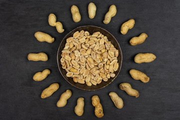 Lot of whole lot of halves of natural yellow peanut in dark ceramic bowl flatlay on grey stone