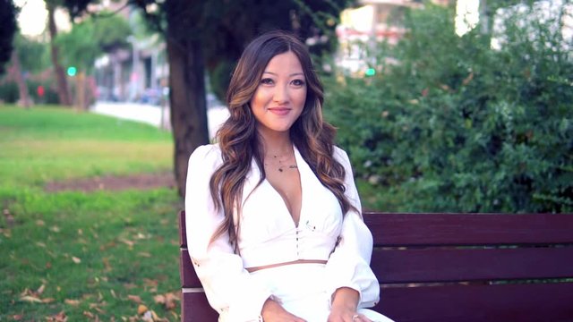 Beautiful Asian girl smiling in the park. She is wearing white dress. Happy video
