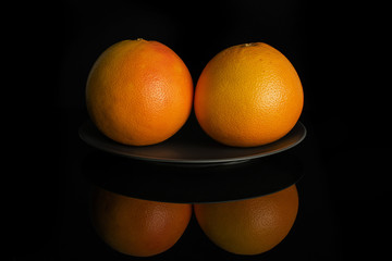 Group of two whole fresh pink grapefruit on gray ceramic plate isolated on black glass
