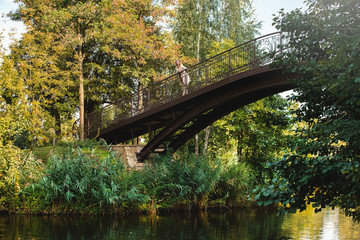 Beautiful and young girl stands on the wooden bridge near the river in the green park . She looks at the beautiful nature.