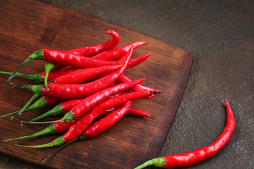 Pods of hot red pepper on a wooden board on a rusty metal surface.