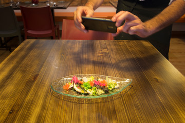 chef photographing in motion his creation, a beautiful salad with sardine loins