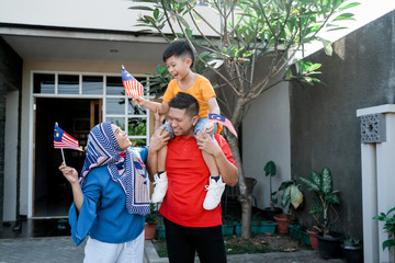 proud malaysian family holding malaysia flag in front of their house on independence day