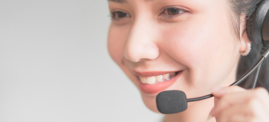 Smiling Asian woman consultant wearing microphone headset of customer support phone operator at...