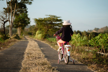 Fototapeta premium back view of a child riding a bicycle in country side road by her self