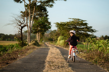 Obraz premium independent asian child ride her bicycle in countryside road by her self with beautiful scenery and sunset