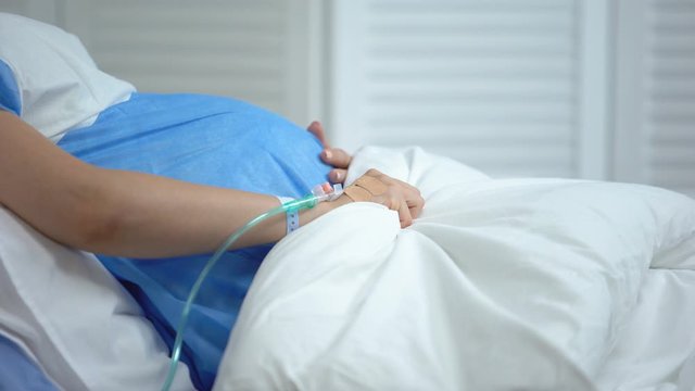 Pregnant woman holding blanket, feeling abdominal pain, risk of miscarriage