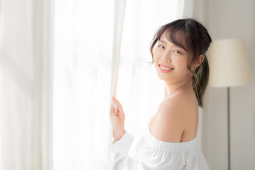 Fototapeta na wymiar Portrait of beautiful young asian woman standing the window and smile while wake up with sunrise at morning, girl happy with freshness and cheerful, lifestyle and relax concept.