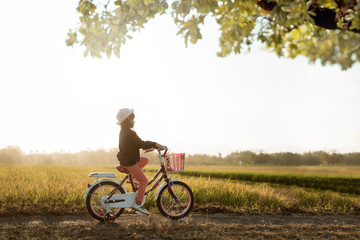 Fototapeta premium independent asian child ride her bicycle in countryside road by her self with beautiful scenery and sunset