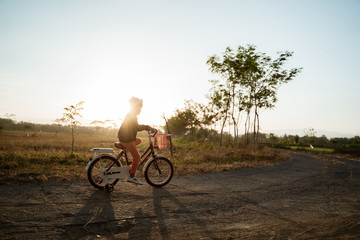 Fototapeta premium independent asian child ride her bicycle in countryside road by her self with beautiful scenery and sunset