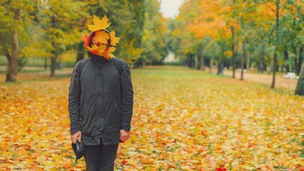 Strange hipster man in black parka jacket with fall leaves on face standing in autumn park. Funny...