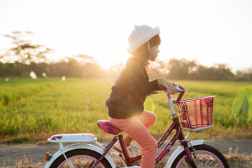 independent asian child ride her bicycle in countryside road by her self with beautiful scenery and sunset