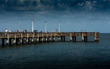 Fototapeta na wymiar Fishing Pier With Storm Clouds Rolling In on People fishing