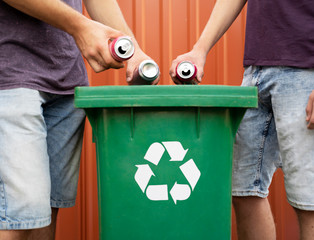 Men putting tin cans in recycle bin, outdoors 