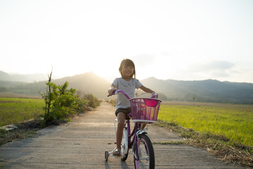 Obraz premium independent asian child ride her bicycle in countryside road by her self with beautiful scenery and sunset